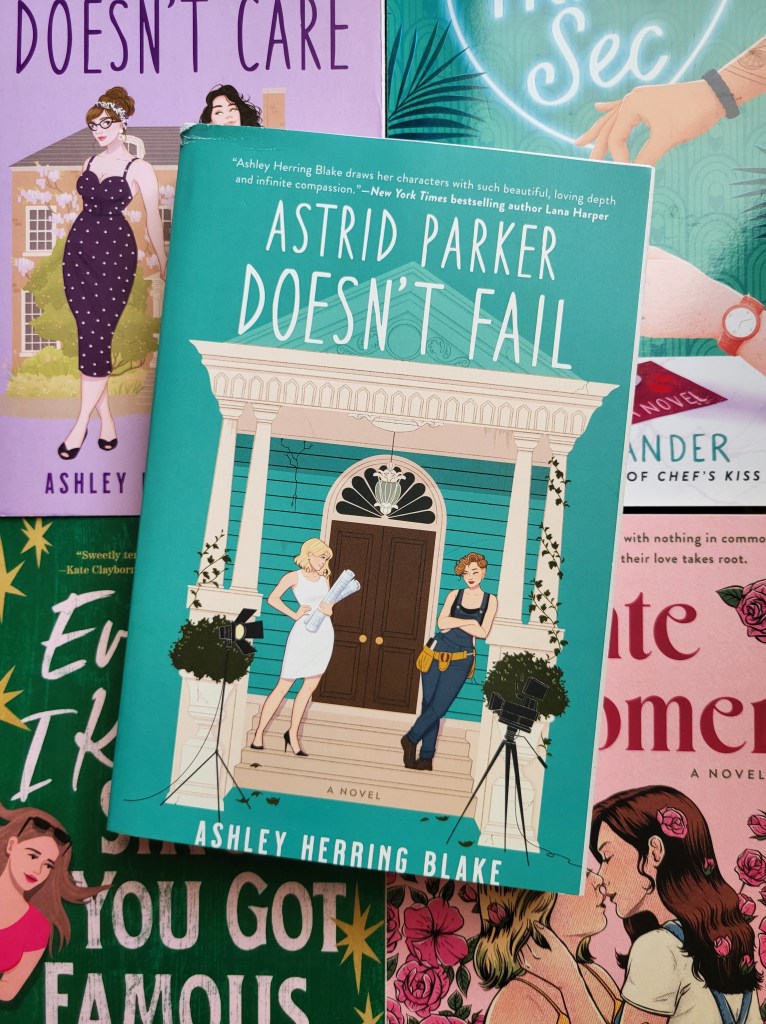 photo of Astrid Parker Doesn't Fail book (turquoise background, with a white porch of a house. Two women, one in a white dress and one in overalls, stand on the porch steps, looking at each other). The book is on top of several other sapphic romance books (Delilah Green Doesn't Care, Triple Sec, Everyone I Kissed Since You Got Famous, and Late Bloomer) to create a pastel background.