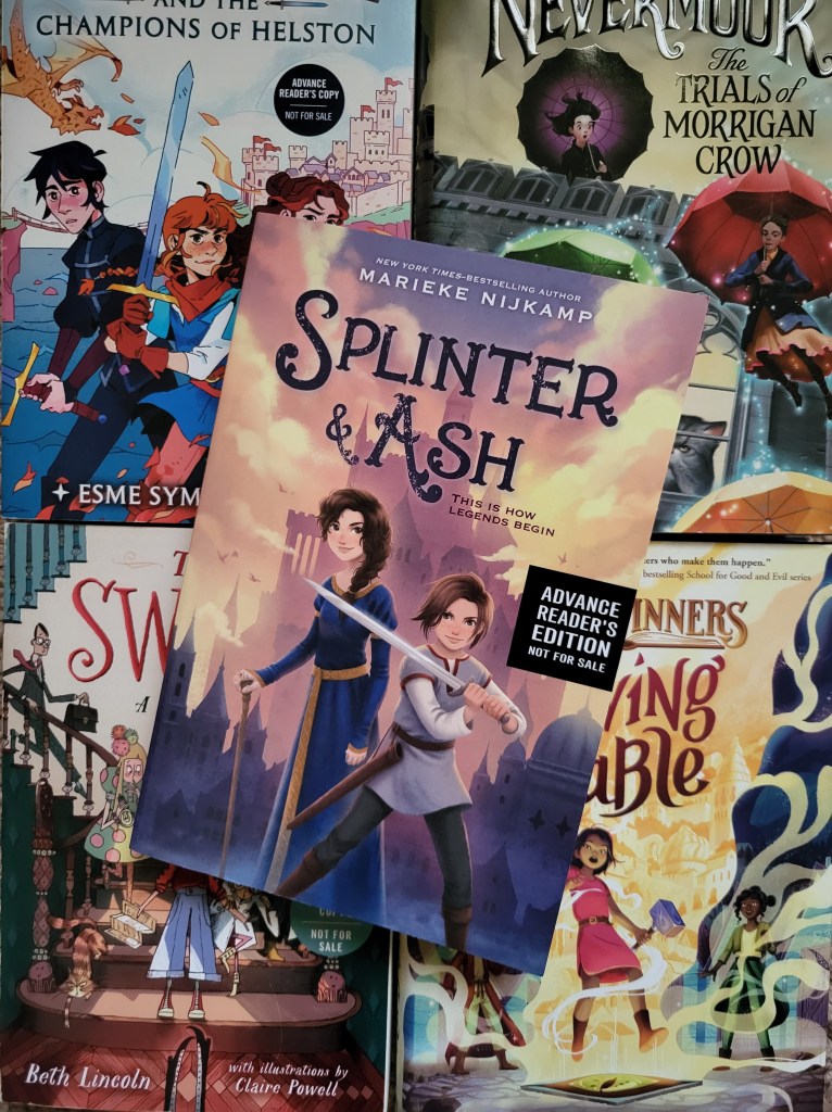 photo of Splinter and Ash: the cover depicts two tweens, one in a blue dress holding a cane and the other in a gray tunic holding a sword. A castle stands behind them. The book itself sits on other middle grade titles (Sir Callie, Nevermoor, The Swifts, and Saving Fable)