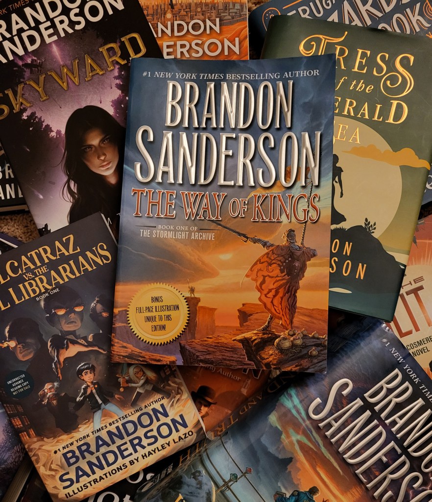 photo the Way of Kings: the cover depicts two figures in armor, facing each other from different plateaus on a barren landscape. The book itself sits on a pile of other books by the same author.