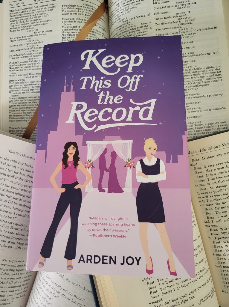 photo of Keep This Off the Record: a purple background with a city skyline, with a wedding altar in the center. Who people stand under it, holding hands. In the foreground, two women stand, looking at each other askance. One has long dark hair, the other blonde.