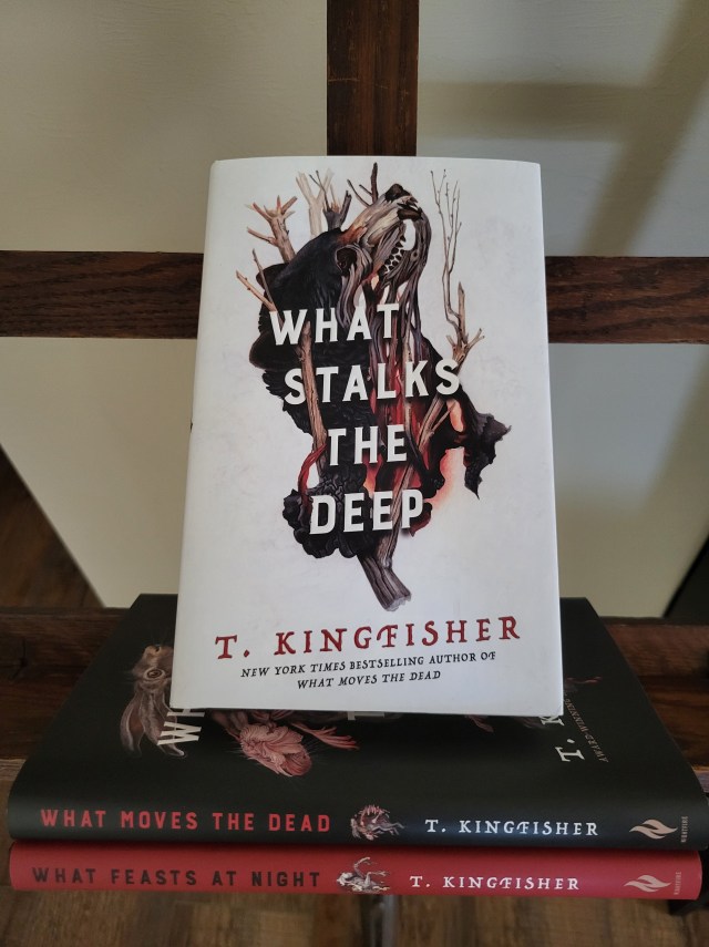 photo of What Stalks the Deep: a white background, on which there is a bear-like creature, with sticks and branches seemingly growing within and out of it. The title is in white letters atop this image. The book itself sits atop the other two in the series.