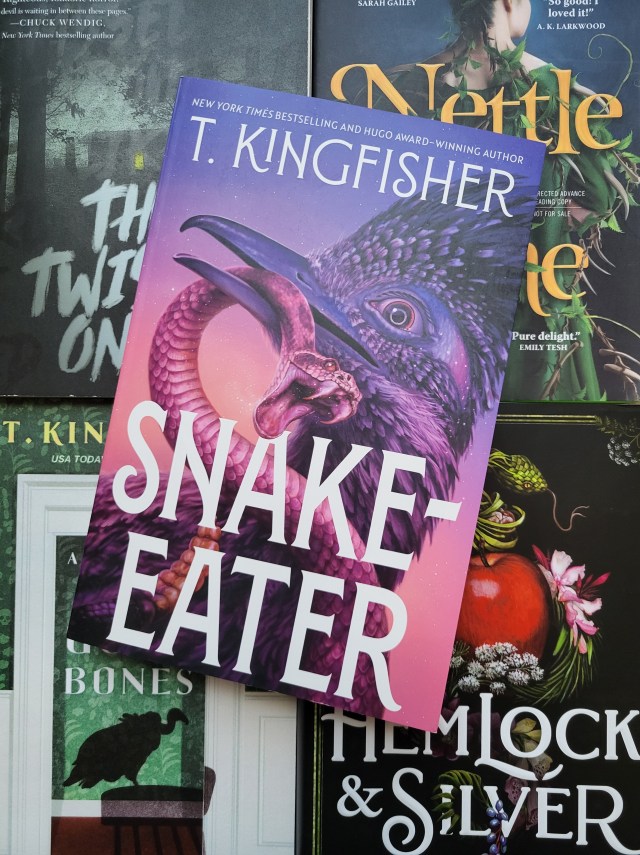 photo of Snake-Eater: a roadrunner clutches a rattlesnake in its beak. The title and author name are in white text over the image. The book itself sits on other Kingfisher titles (The Twisted Ones, Nettle & Bone, A House With Good Bones, and Hemlock & Silver)